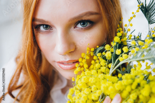 Portrait of a red-haired beautiful girl with a Mimosa in a long white dress