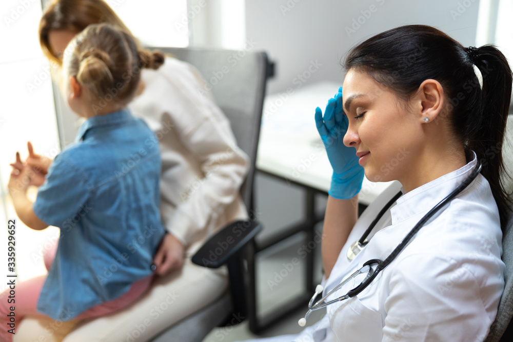 Fototapeta premium Tired female doctor with stethoscope on shoulders having rest