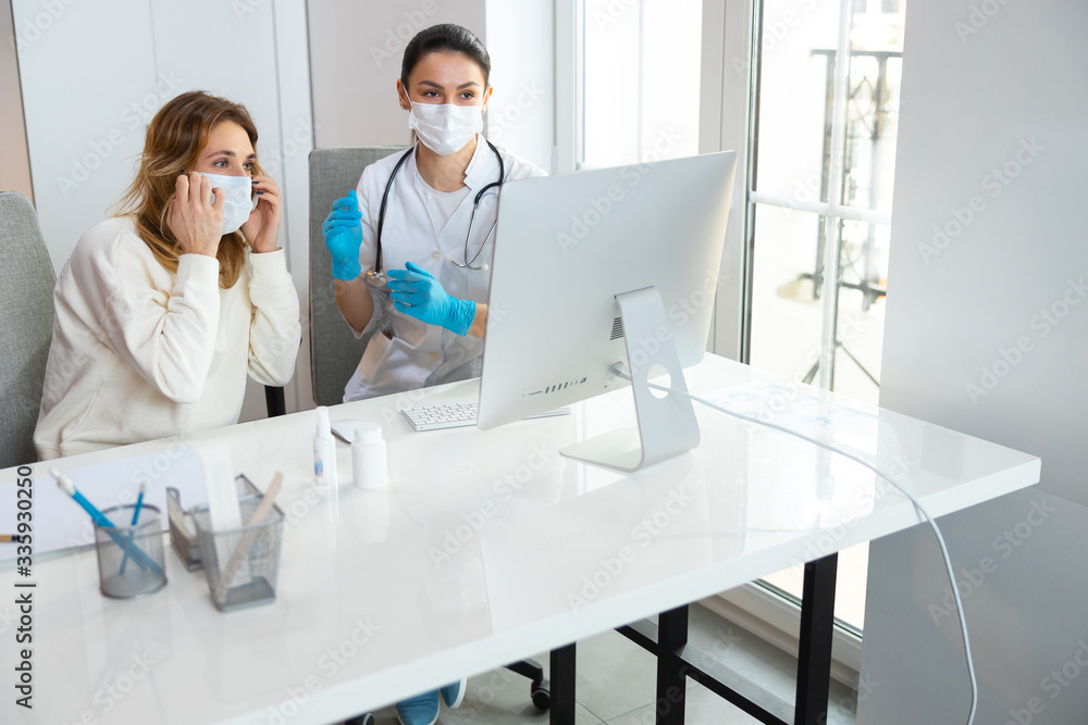 Fototapeta premium Caucasian women in medical mask looking at screen of laptop in hospital