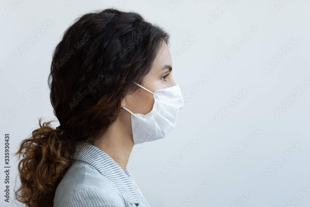 Side view head shot young woman wearing air pollution protective mask, responsible lady with covered mouth nose medical respirator looking on free copy space for text, stop spread virus advertising.