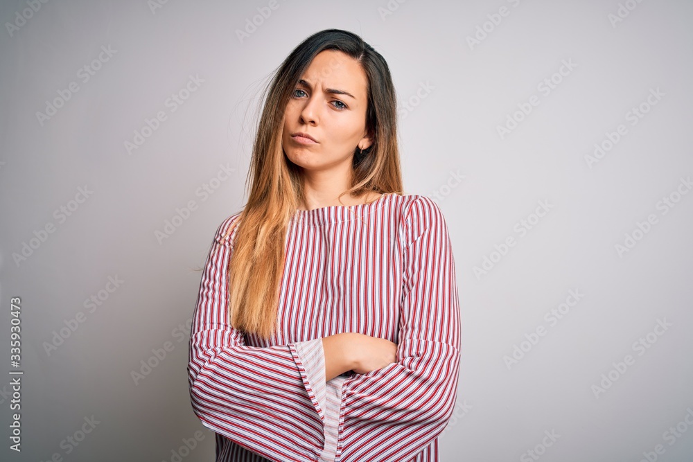 Young beautiful blonde woman with blue eyes wearing stiped t-shirt over white background skeptic and nervous, disapproving expression on face with crossed arms. Negative person. Young beautiful blonde woman with blue eyes wearing stiped t-shirt over white background skeptic and nervous, disapproving expression on face with crossed arms. Negative person.