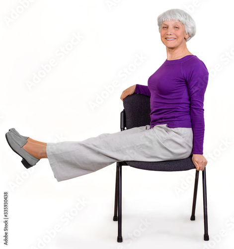 Happy charming beautiful elderly woman doing exercises at home on a chair. Workout gymnastics for health. On a white background