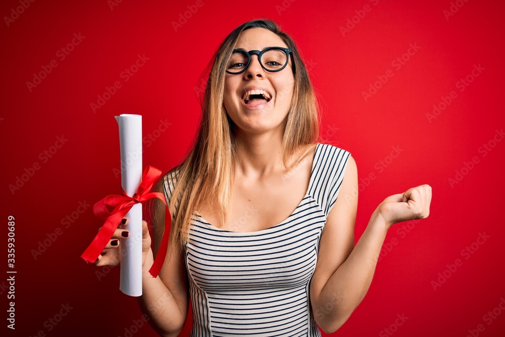 Young blonde woman with blue eyes wearing glasses holding graduated degree diploma screaming proud and celebrating victory and success very excited, cheering emotion Young blonde woman with blue eyes wearing glasses holding graduated degree diploma screaming proud and celebrating victory and success very excited, cheering emotion