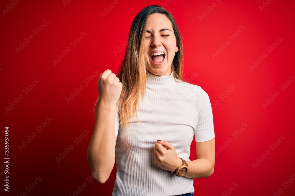 Beautiful blonde woman with blue eyes wearing casual white t-shirt over red background celebrating surprised and amazed for success with arms raised and eyes closed. Winner concept. Beautiful blonde woman with blue eyes wearing casual white t-shirt over red background celebrating surprised and amazed for success with arms raised and eyes closed. Winner concept.