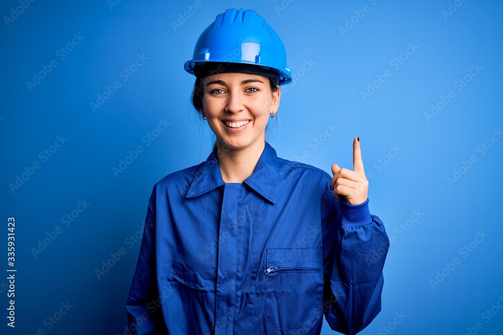 Young beautiful worker woman with blue eyes wearing security helmet and uniform pointing finger up with successful idea. Exited and happy. Number one. Young beautiful worker woman with blue eyes wearing security helmet and uniform pointing finger up with successful idea. Exited and happy. Number one.