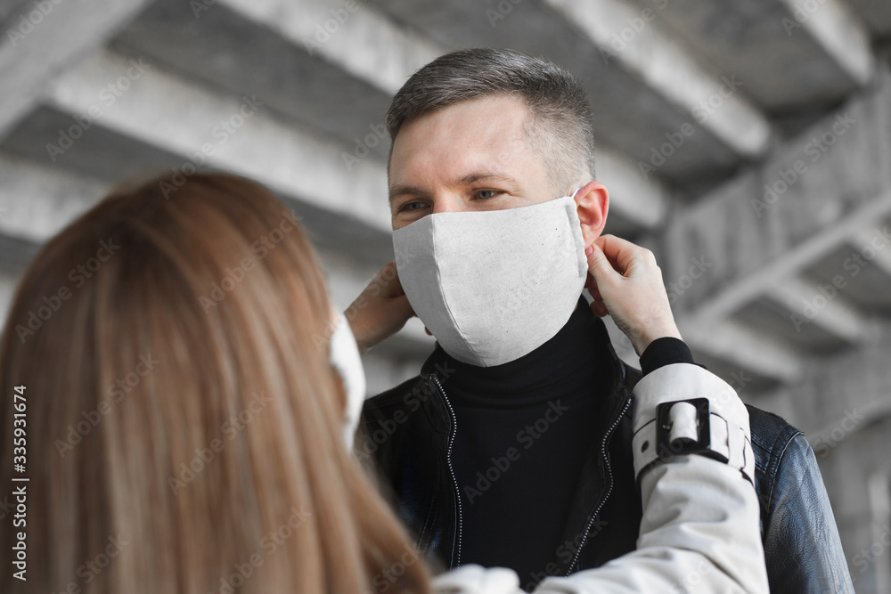 A woman puts a protective mask on a man's face. Coronavirus, covid19