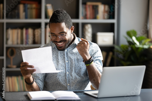 Overjoyed African American male student feel euphoric read good news in paperwork letter, excited biracial man triumph get positive answer reply in paper postal correspondence, success concept
