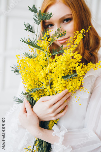 Portrait of a red-haired beautiful girl with a Mimosa in a long white dress
