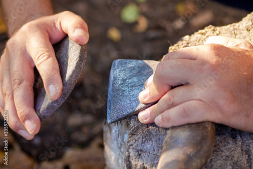 A man sharpens an axe with a whetstone. Weapon.