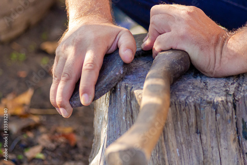 A man sharpens an axe with a whetstone. Weapon.