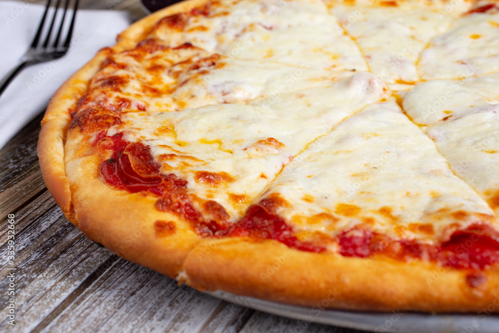 A view of an extra cheesy pizza, in a restaurant or kitchen setting.