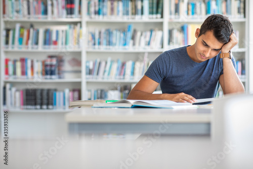Students in a library - handsome student reading a book for his class in a bright modern library