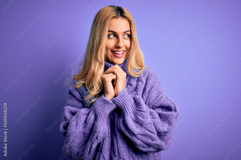 Young beautiful blonde woman wearing casual turtleneck sweater over purple background laughing nervous and excited with hands on chin looking to the side Young beautiful blonde woman wearing casual turtleneck sweater over purple background laughing nervous and excited with hands on chin looking to the side