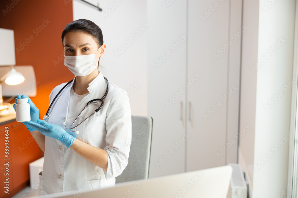 Caucasian doctor in medical mask showing bottle with medicine Caucasian doctor in medical mask showing bottle with medicine