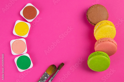 Makarons on a pink background are next to the colors of macaroons and brushes for drawing photo