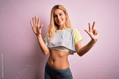 Young beautiful blonde sportswoman doing sport wearing sportswear over pink background showing and pointing up with fingers number eight while smiling confident and happy.