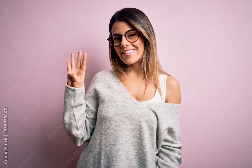Young beautiful brunette woman wearing casual sweater and glasses over pink background showing and pointing up with fingers number four while smiling confident and happy. Young beautiful brunette woman wearing casual sweater and glasses over pink background showing and pointing up with fingers number four while smiling confident and happy.