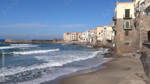 Beautiful empty beach, blue sea with white waves, old historical houses in the recreational city Cefalu on Sicily island, Italy 