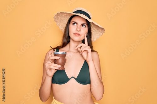 Young beautiful girl wearing swimwear bikini and summer hat drinking traditional mate drink serious face thinking about question, very confused idea