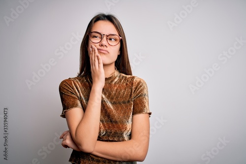 Young beautiful brunette girl wearing casual t-shirt and glasses over isolated white background with hand on chin thinking about question, pensive expression. Smiling with thoughtful face. Doubt © Krakenimages.com