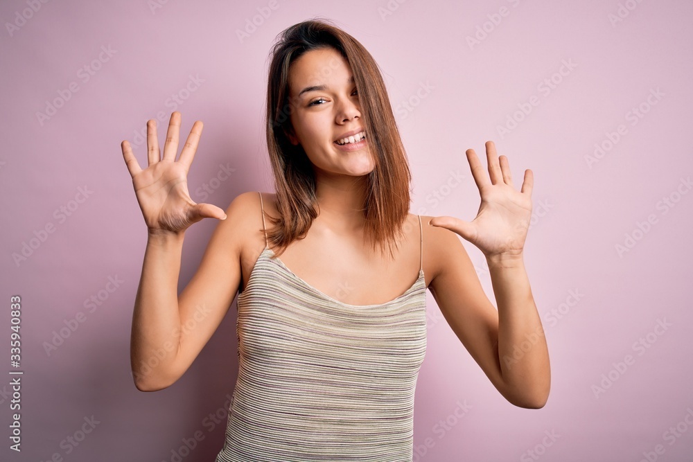 Young beautiful brunette girl wearing casual striped t-shirt over isolated pink background showing and pointing up with fingers number ten while smiling confident and happy. Young beautiful brunette girl wearing casual striped t-shirt over isolated pink background showing and pointing up with fingers number ten while smiling confident and happy.