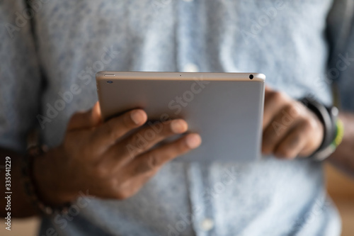 Close up of African American man browsing surfing wireless Internet on modern tablet gadget, focused biracial male texting or messaging, read news or check male on pad device, technology concept