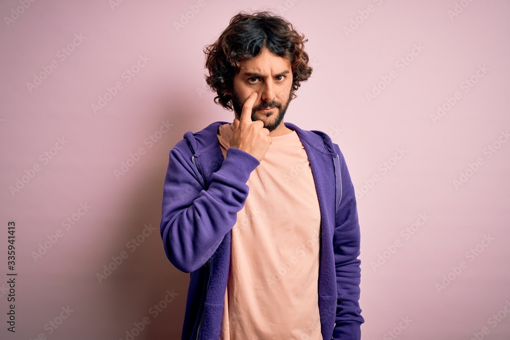 Young handsome sporty man with beard wearing casual sweatshirt over pink background Pointing to the eye watching you gesture, suspicious expression Young handsome sporty man with beard wearing casual sweatshirt over pink background Pointing to the eye watching you gesture, suspicious expression