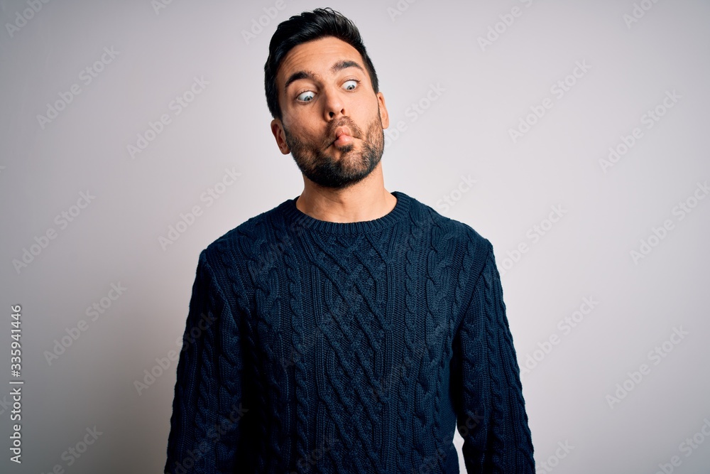 Obraz premium Young handsome man with beard wearing casual sweater standing over white background making fish face with lips, crazy and comical gesture. Funny expression.