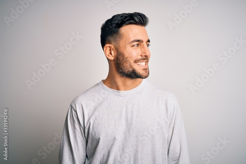 Young handsome man wearing casual t-shirt standing over isolated white background looking away to side with smile on face, natural expression. Laughing confident.