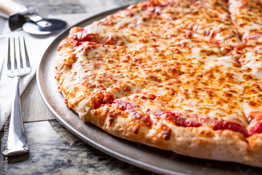 A closeup view of a plain cheese pizza pie cut off on the right side of the frame, in a restaurant or kitchen setting. A closeup view of a plain cheese pizza pie cut off on the right side of the frame, in a restaurant or kitchen setting.
