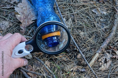 Wallpaper Mural magnifier in hand magnifies an empty blue plastic bottle on dry leaves and needles in the forest on nature Torontodigital.ca