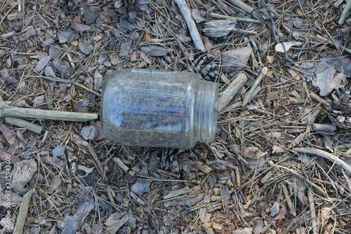 one dirty empty glass jar lies on dry grass and earth on nature