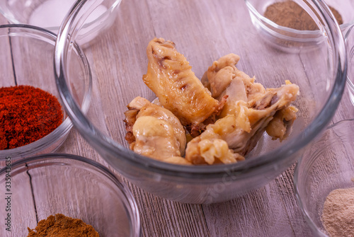 Glass bowl of chicken wings surrounded by glass bowls of spices