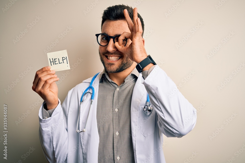 Young doctor man wearing stethoscope holding help note over isolated background with happy face smiling doing ok sign with hand on eye looking through fingers Young doctor man wearing stethoscope holding help note over isolated background with happy face smiling doing ok sign with hand on eye looking through fingers