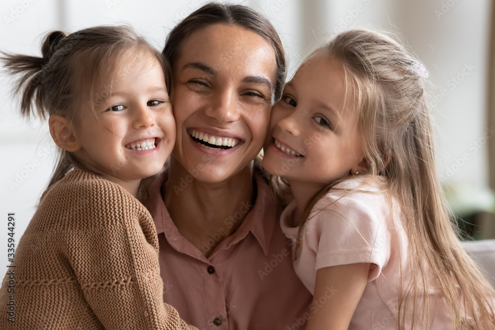 Head shot close up young mixed race woman nanny babysitter touching cheeks with cute little children kids, looking at camera. Portrait of young mother enjoying sweet tender moment with daughters. Head shot close up young mixed race woman nanny babysitter touching cheeks with cute little children kids, looking at camera. Portrait of young mother enjoying sweet tender moment with daughters.