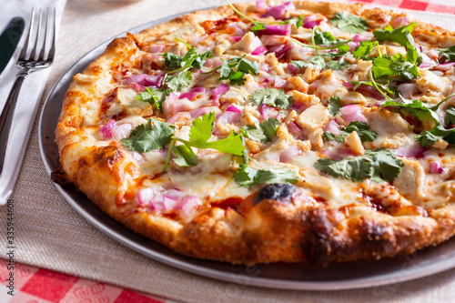 A view of a rustic pizza with chicken and cilantro, in a restaurant or kitchen setting.