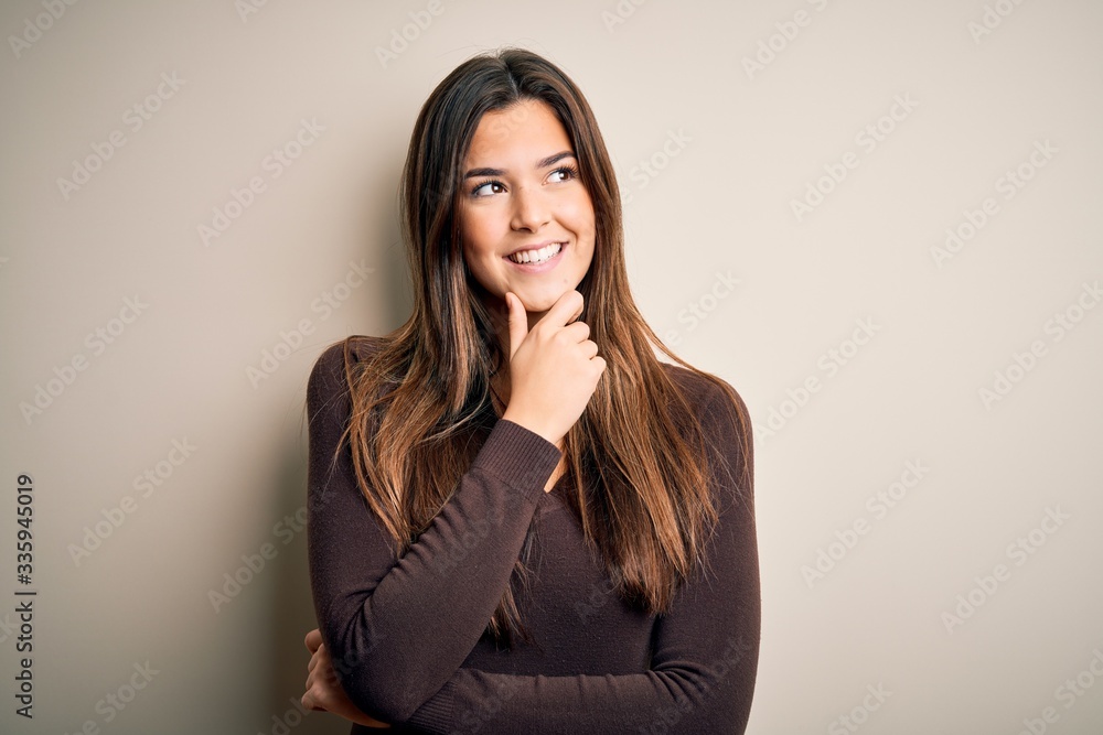Young beautiful girl wearing casual sweater standing over isolated white background with hand on chin thinking about question, pensive expression. Smiling with thoughtful face. Doubt concept. Young beautiful girl wearing casual sweater standing over isolated white background with hand on chin thinking about question, pensive expression. Smiling with thoughtful face. Doubt concept.