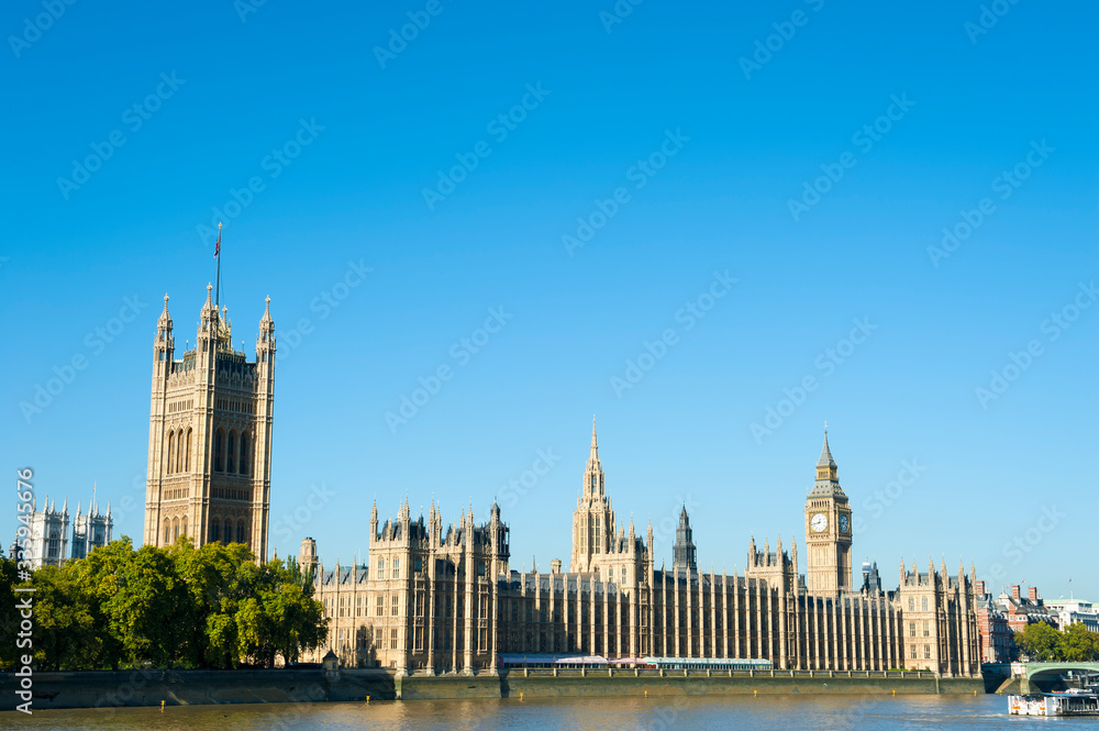 Bright scenic view of the Houses of Parliament in Westminster from the south bank of the River Thames under clear blue sky in London, UK 