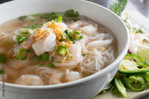 A closeup view of a big bowl of shrimp pho, in a restaurant or kitchen setting.