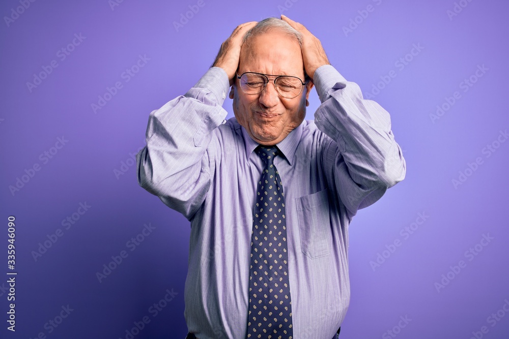 Grey haired senior business man wearing glasses standing over purple isolated background suffering from headache desperate and stressed because pain and migraine. Hands on head. Grey haired senior business man wearing glasses standing over purple isolated background suffering from headache desperate and stressed because pain and migraine. Hands on head.