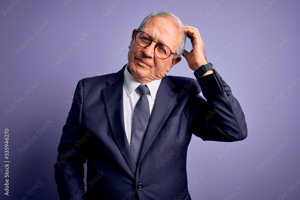 Grey haired senior business man wearing glasses and elegant suit and tie over purple background confuse and wondering about question. Uncertain with doubt, thinking with hand on head. Pensive concept.