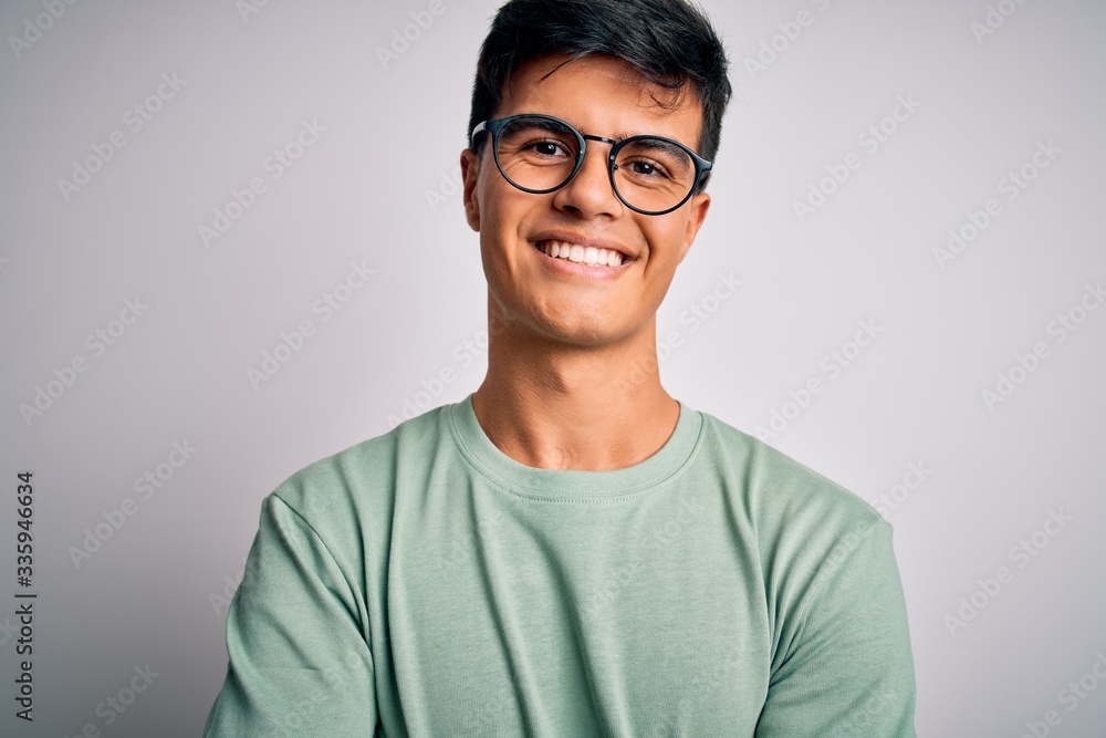 Young handsome man wearing casual t-shirt and glasses over isolated white background happy face smiling with crossed arms looking at the camera. Positive person.