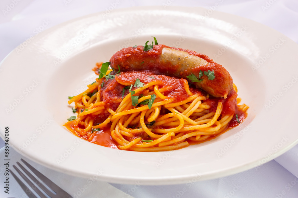 A view of a bowl of spaghetti and Italian sausage, in a restaurant or kitchen setting. A view of a bowl of spaghetti and Italian sausage, in a restaurant or kitchen setting.