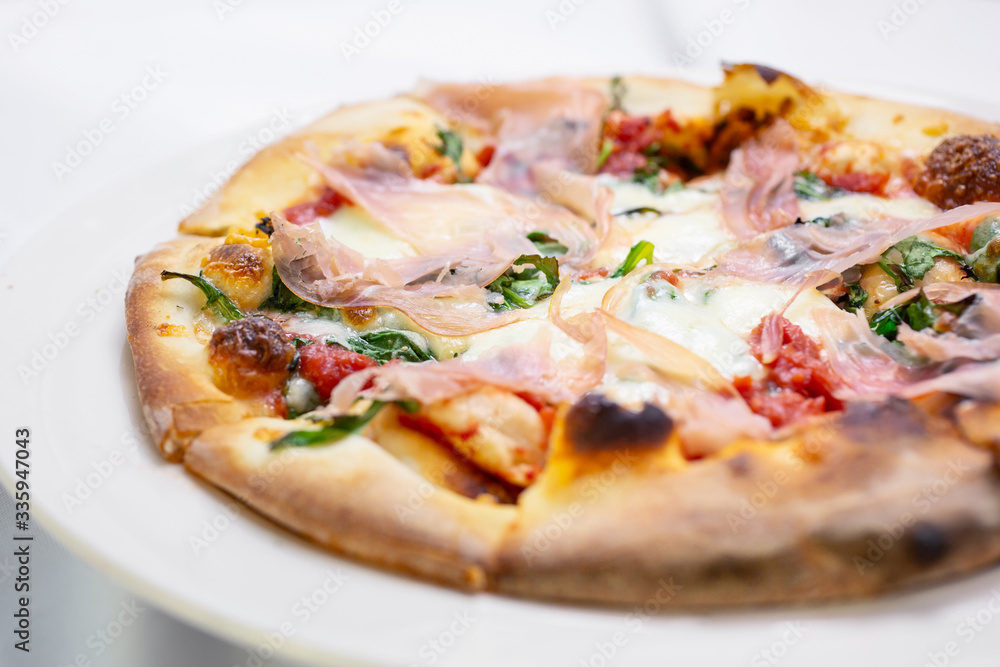 A closeup view of a pizza pie with prosciutto toppings, in a restaurant or kitchen setting. A closeup view of a pizza pie with prosciutto toppings, in a restaurant or kitchen setting.