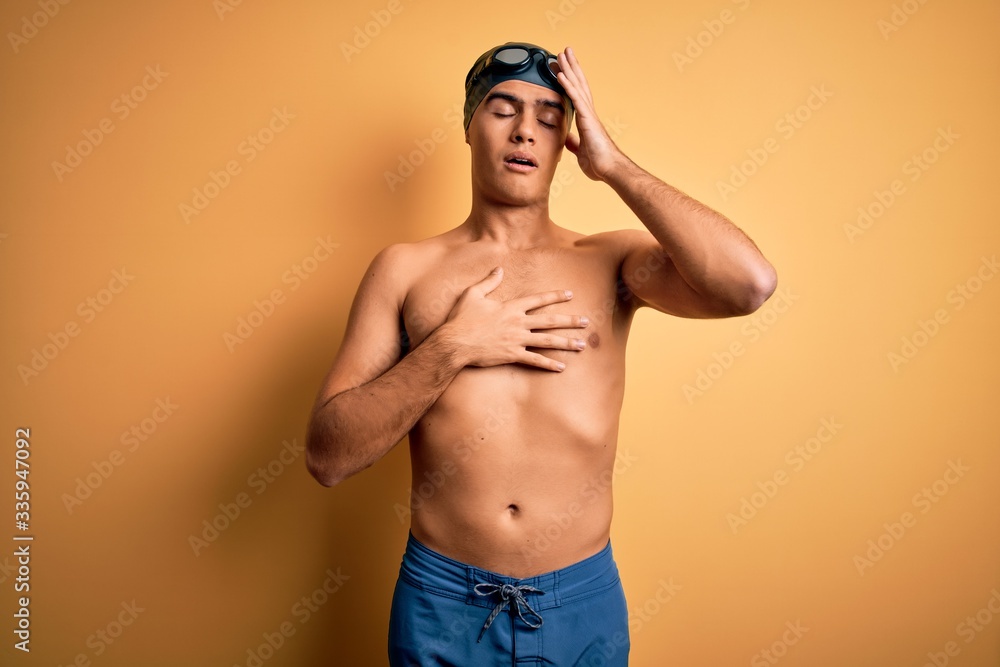 Young handsome man shirtless wearing swimsuit and swim cap over isolated yellow background Touching forehead for illness and fever, flu and cold, virus sick