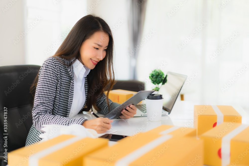 Portrait beautiful young asian business woman work from home with laptop mobile phone with cardboard box ready for shipping Portrait beautiful young asian business woman work from home with laptop mobile phone with cardboard box ready for shipping