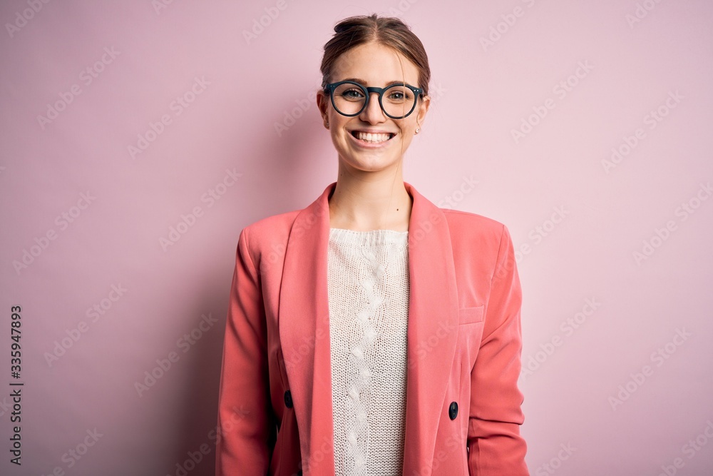 Young beautiful redhead woman wearing jacket and glasses over isolated pink background with a happy and cool smile on face. Lucky person.