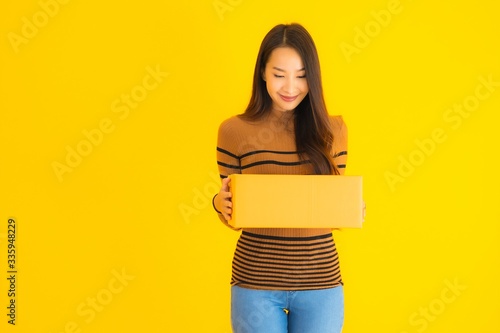 Beautiful young asian woman holding cardboard box in her hand on yellow background