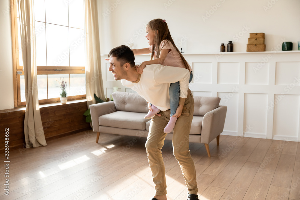 Full length happy father giving piggyback ride to overjoyed little preschool daughter. Excited small child girl having fun playing with energetic young daddy, enjoying active game in living room. Full length happy father giving piggyback ride to overjoyed little preschool daughter. Excited small child girl having fun playing with energetic young daddy, enjoying active game in living room.