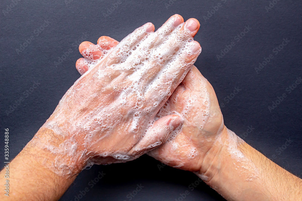 A person washing hands with soap on a black background